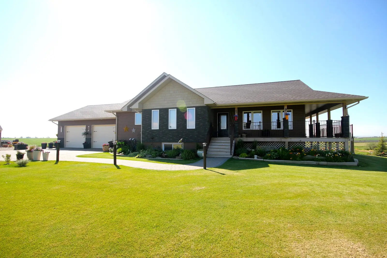 Spacious RTM home with attached double garage, dark stone and siding exterior, large covered wraparound porch, and landscaped front yard with bright green lawn.