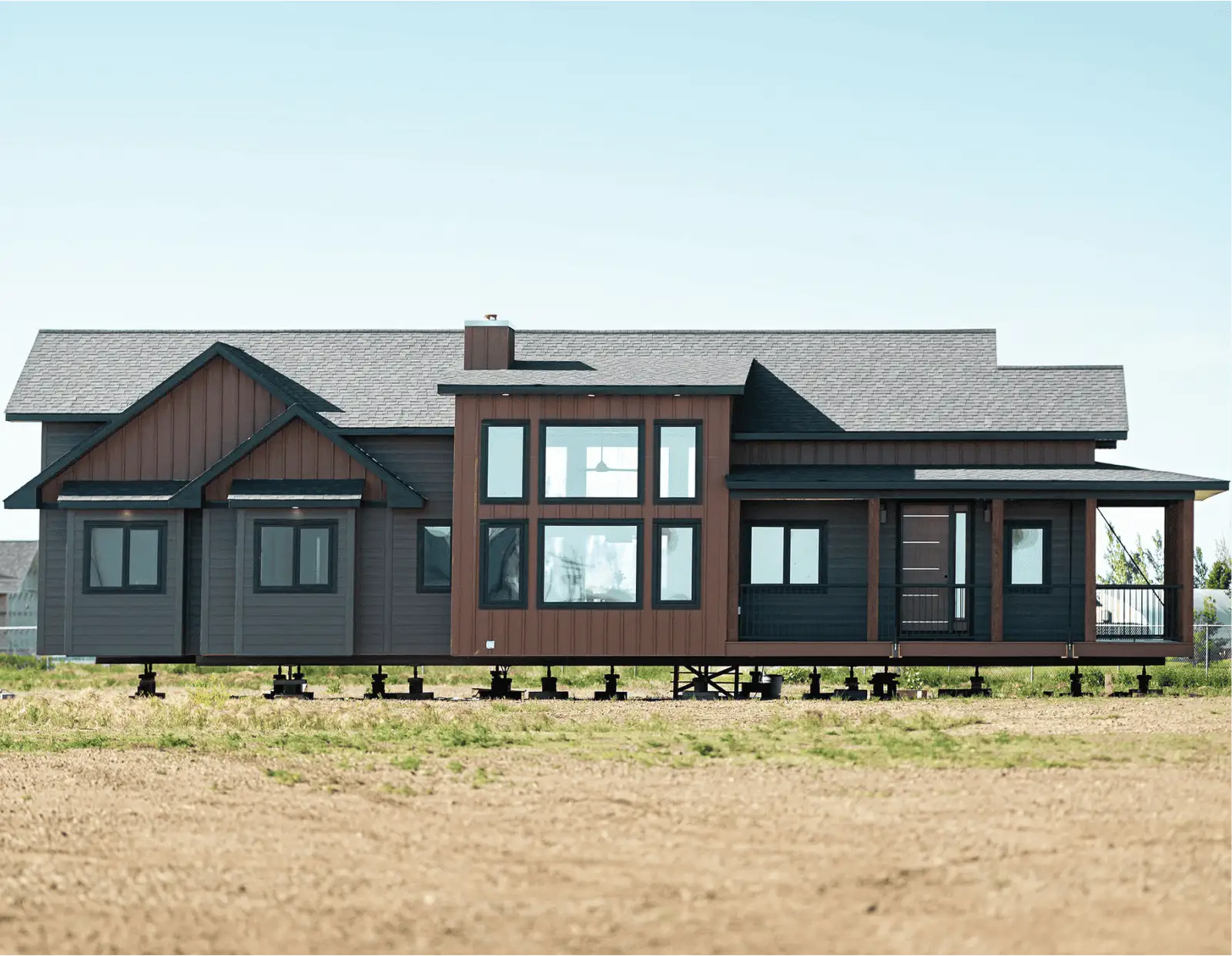 Ready-to-move home elevated on blocks with modern two-tone siding, large grid windows, multiple gables, and a covered front porch.