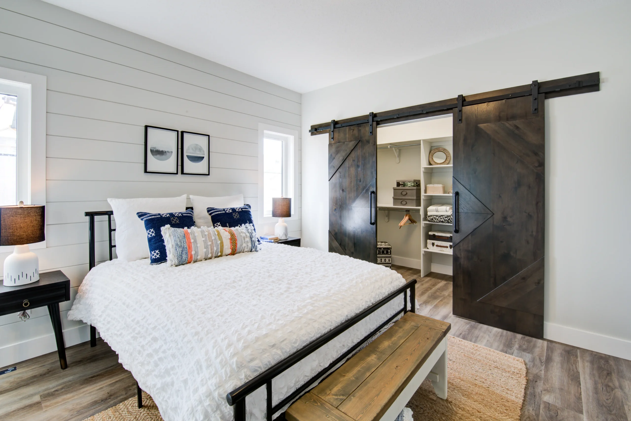 Modern RTM home bedroom with white shiplap accent wall, cozy bedding, rustic barn-style sliding doors, and a spacious walk-in closet with built-in shelving.