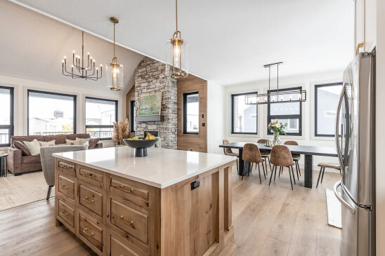 Open concept RTM home interior with quartz kitchen island, stone fireplace and vaulted ceiling in Alberta and Saskatchewan