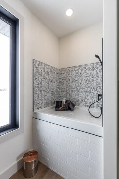 Built-in dog wash station with tiled backsplash and handheld shower in custom RTM home in Alberta and Saskatchewan