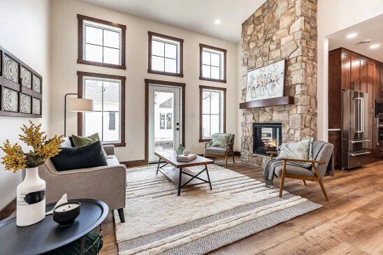 Bright living room in an RTM home with tall windows, stone fireplace, modern sofa, accent chairs, and a textured area rug.