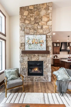 Stone fireplace feature wall in an RTM home with a built-in gas fireplace, floral artwork above the mantel, and cozy accent chairs on either side.