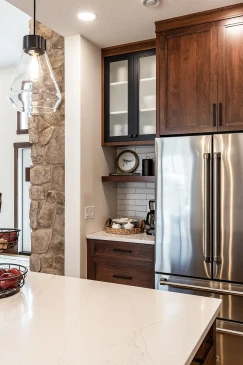 Close-up of modern kitchen corner with stainless steel French door fridge, wood cabinets, white subway tile backsplash, open shelves, and a coffee station.