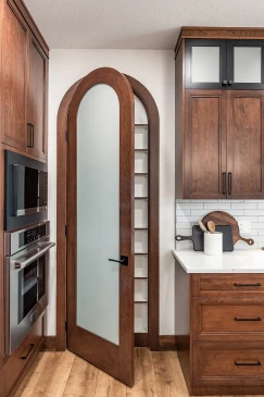 Kitchen view with arched frosted glass pantry door, surrounded by dark wood cabinets, stainless steel oven and microwave, and subway tile backsplash with countertop decor.