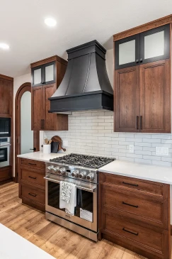 Modern kitchen with stainless steel gas range, large black range hood, subway tile backsplash, and dark wood cabinetry with quartz countertops.