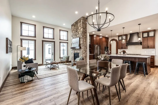 Bright open-concept home with dining area, stone fireplace, large windows, and modern kitchen with island and pendant lighting.
