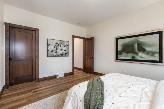 Bedroom with white walls, wood trim and doors, a bed with white bedding and green throw blanket, and wall art featuring floral and abstract designs.