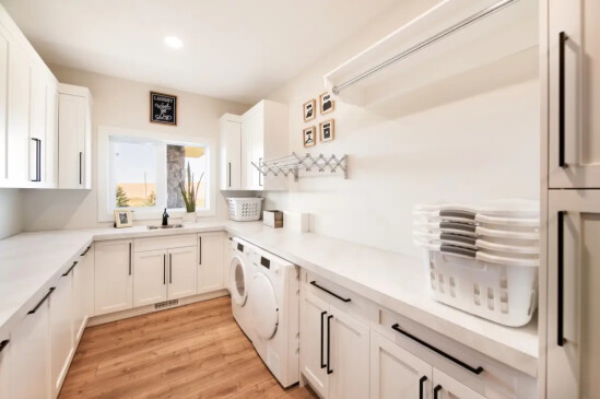 Functional laundry room with extensive cabinetry, folding counters, utility sink, and built in storage.