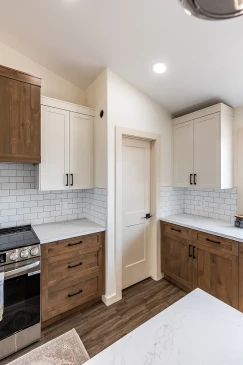 Bright kitchen featuring white upper cabinets, wood lower cabinets with black handles, subway tile backsplash, and quartz countertops, showcasing a clean and modern farmhouse style in a Saskatchewan ready-to-move home.