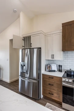 Modern kitchen with stainless steel French door refrigerator, white upper cabinets, wood lower drawers, subway tile backsplash, and a gas range, inside a Saskatchewan ready-to-move home.