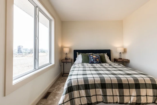 Bright bedroom in a ready-to-move home featuring a checkered bedspread, decorative pillows, matching bedside tables with lamps, and a large window letting in natural light.