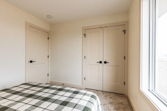 Cozy bedroom in a ready-to-move home featuring a checkered bedspread, double closet doors, and a large window letting in natural light.