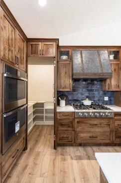 Custom RTM home kitchen with gas cooktop, rustic wood cabinetry, blue tile backsplash, and a farmhouse-style vent hood.
