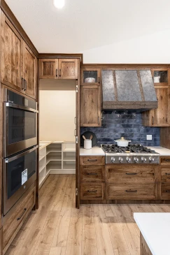 Custom RTM home kitchen with gas cooktop, rustic wood cabinetry, blue tile backsplash, and a farmhouse-style vent hood.