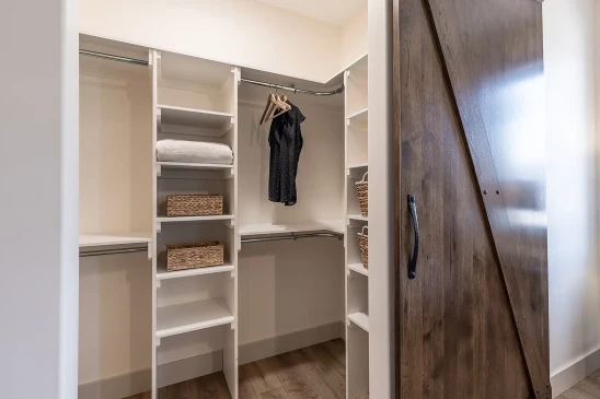 Organized walk-in closet with built-in white shelving, wicker baskets, and hanging space beside a rustic wood barn door.