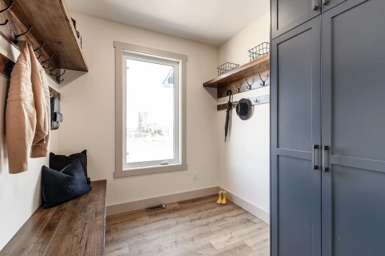 Bright mudroom with navy blue cabinets, wooden bench, coat hooks, and shelving with storage baskets.