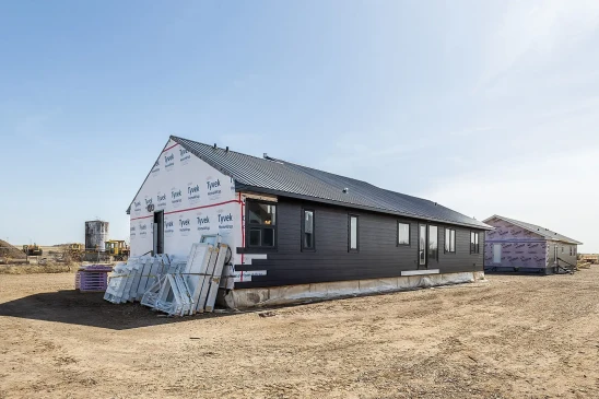 Ready-to-move home under construction with dark siding, black metal roof, and Tyvek house wrap on one side, showcasing the building process in Alberta.