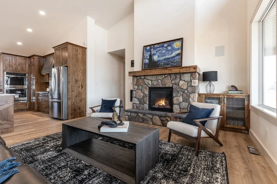 Cozy RTM home living room with stone fireplace, modern wood cabinetry, stainless steel kitchen appliances, and open-concept design with natural light.
