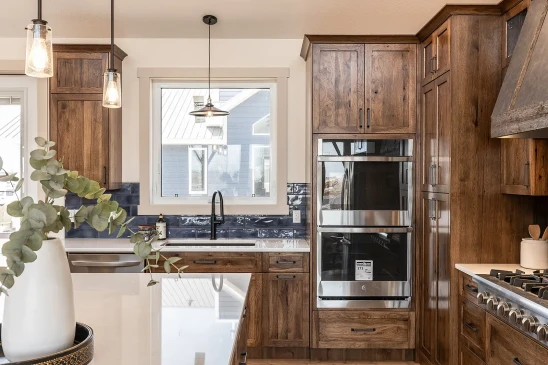 Modern RTM home kitchen with custom wood cabinetry, stainless steel double oven, black faucet, and white quartz countertops.