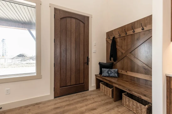 Entryway of an RTM home with a solid wood front door, built-in bench seating, coat hooks, and storage baskets for a functional mudroom design.