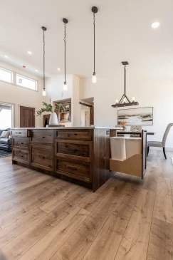 Custom kitchen island with rich wood cabinetry, quartz countertop, pendant lighting, and built-in pull-out garbage bins in a modern RTM home.