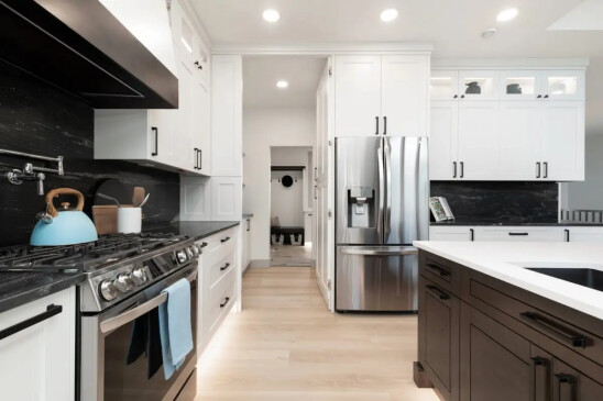 Bright custom kitchen with white cabinetry, black backsplash, quartz countertops, and stainless steel appliances.