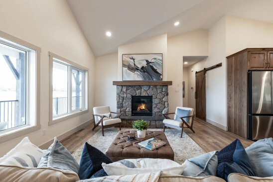 Stone gas fireplace feature wall with wood mantel and modern accent chairs in custom RTM home
