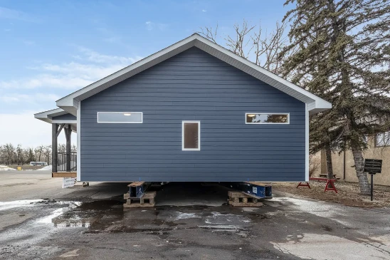 Ready-to-move (RTM) home with navy-blue siding and white trim, set on a foundation of elevated supports. The home features a gabled roof and sleek modern windows, ready for transport to its final location.