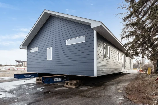Ready-to-move (RTM) home with navy-blue siding and white trim, set on a foundation of elevated supports. The home features a gabled roof and sleek modern windows, ready for transport to its final location.
