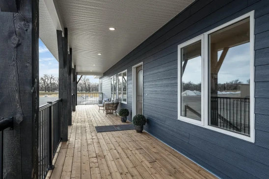 Covered porch with a wooden deck and navy-blue siding, featuring white-framed windows, dark timber posts, and outdoor seating. The space overlooks a serene outdoor setting, creating a welcoming and relaxing environment.